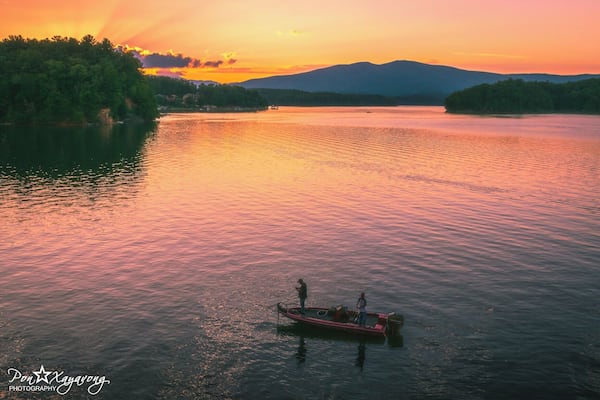 Ein ruhiger See bei Sonnenuntergang, mit einem kleinen Boot und zwei Anglern.