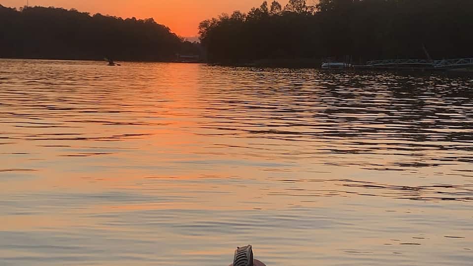 A calm river at sunset with a red kayak in the foreground and a bridge in the background.