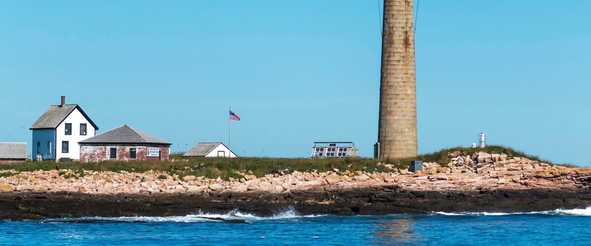 A lighthouse, a rocky shoreline, and a few buildings by the water.