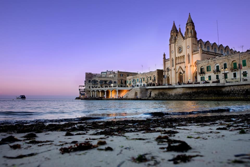 A coastal cityscape with a prominent church and a bridge at dusk.
