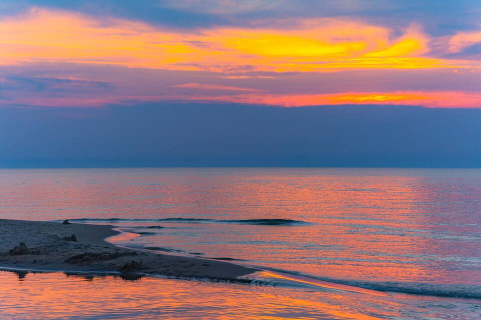 Een strand bij zonsondergang met een rustige zee en een heldere lucht.