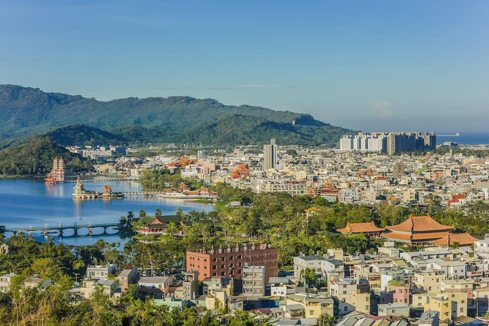 A coastal cityscape with a temple, bridge, and dense urban area.