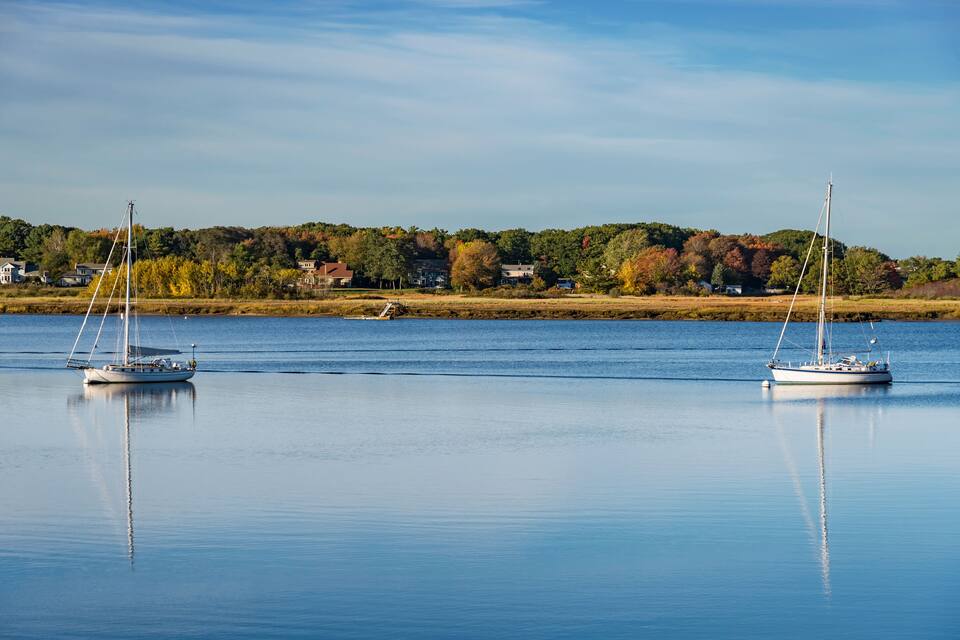 Two sailboats on a calm lake with a forested shoreline in the background.
