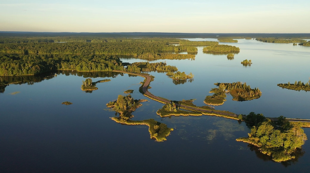 Establishing shot of american wilderness. Aerial view of scenic road through lake, and wooded islands. Calm morning water, dawn sky, view from above.