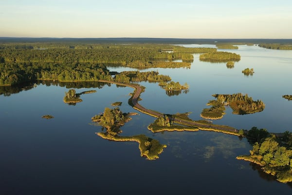 Establishing shot of american wilderness. Aerial view of scenic road through lake, and wooded islands. Calm morning water, dawn sky, view from above.