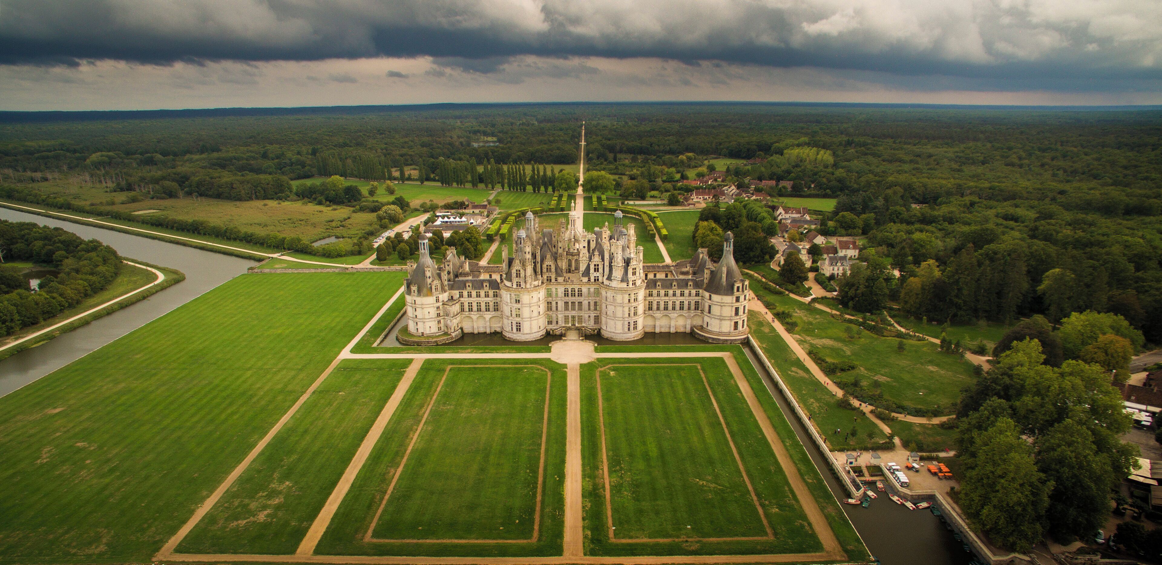 A large, historic castle surrounded by lush green fields and a river.