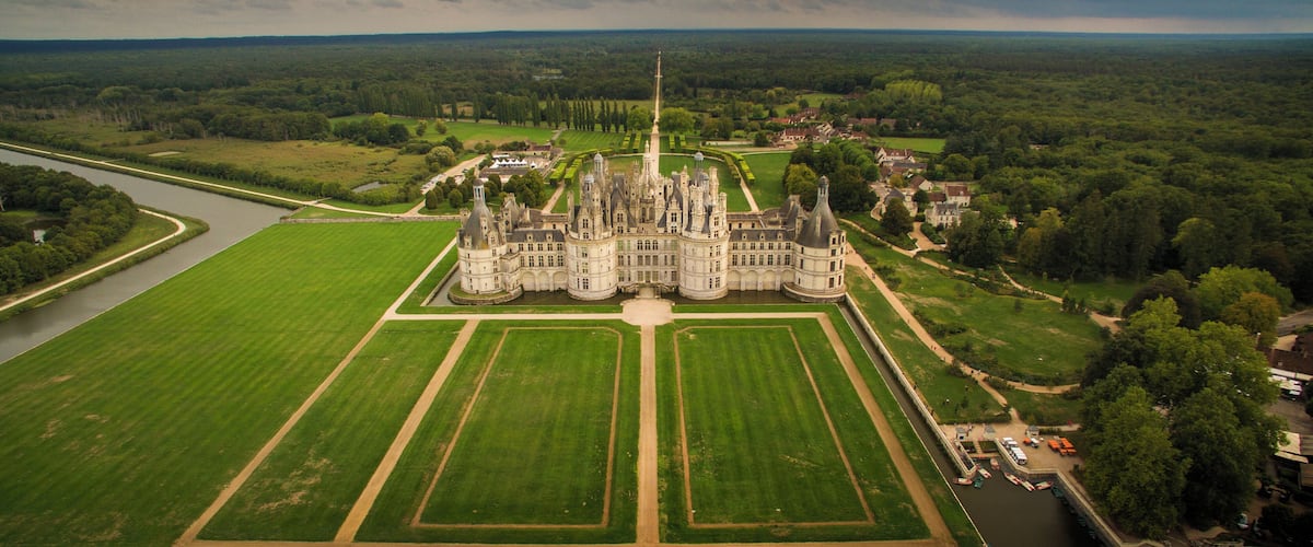 A large, historic castle surrounded by lush green fields and a river.