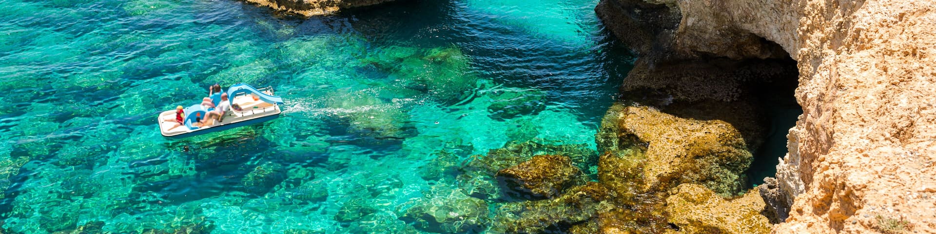 A clear blue sea with a natural rock arch formation and a boat in the water.