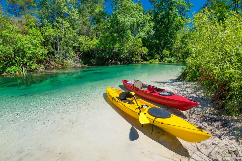 Two kayaks on a sandy beach with clear turquoise water and lush greenery in the background.