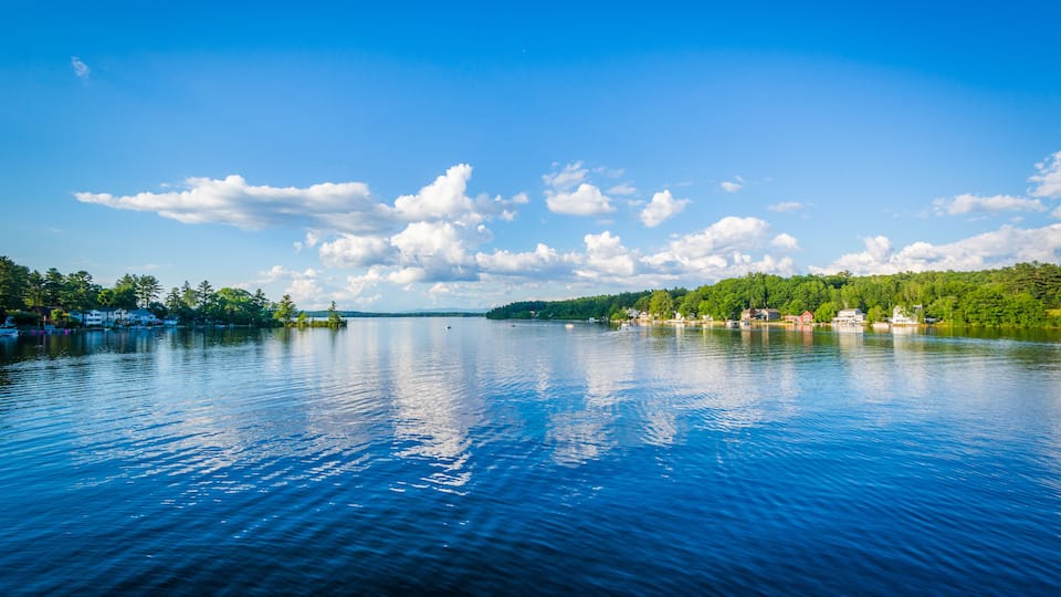 A calm lake with a clear sky, surrounded by green hills and small houses.