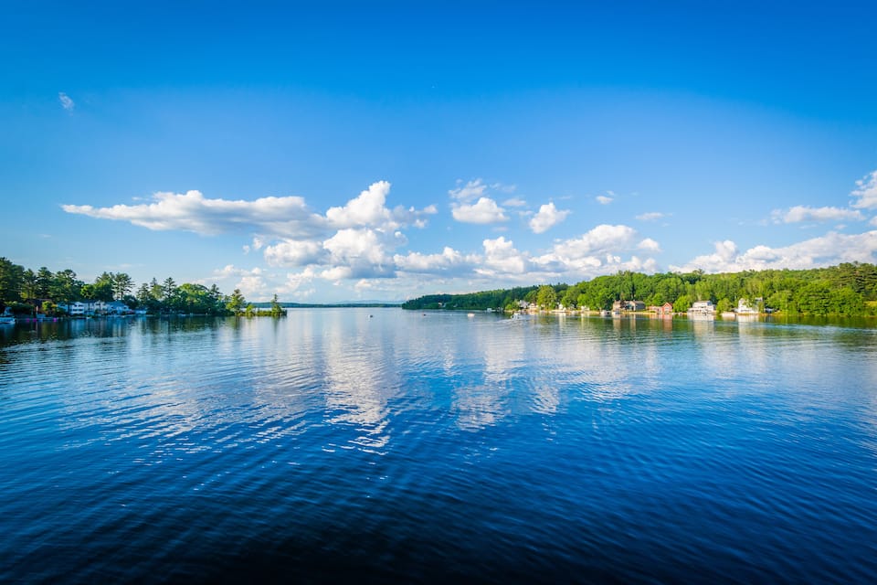 A calm lake with a clear sky, surrounded by green hills and small houses.