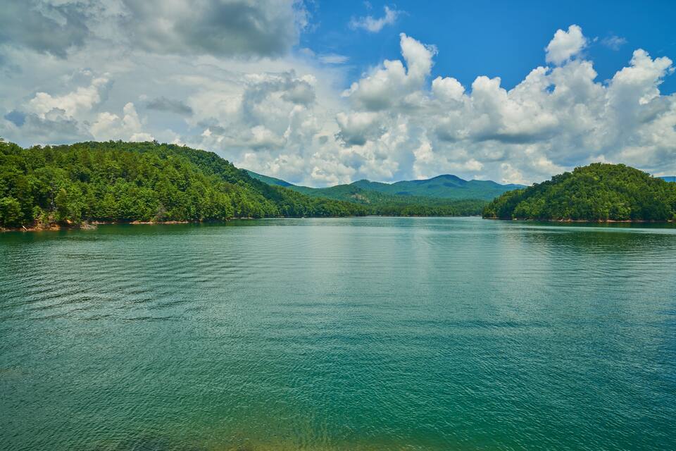 A calm lake surrounded by lush green hills under a partly cloudy sky.