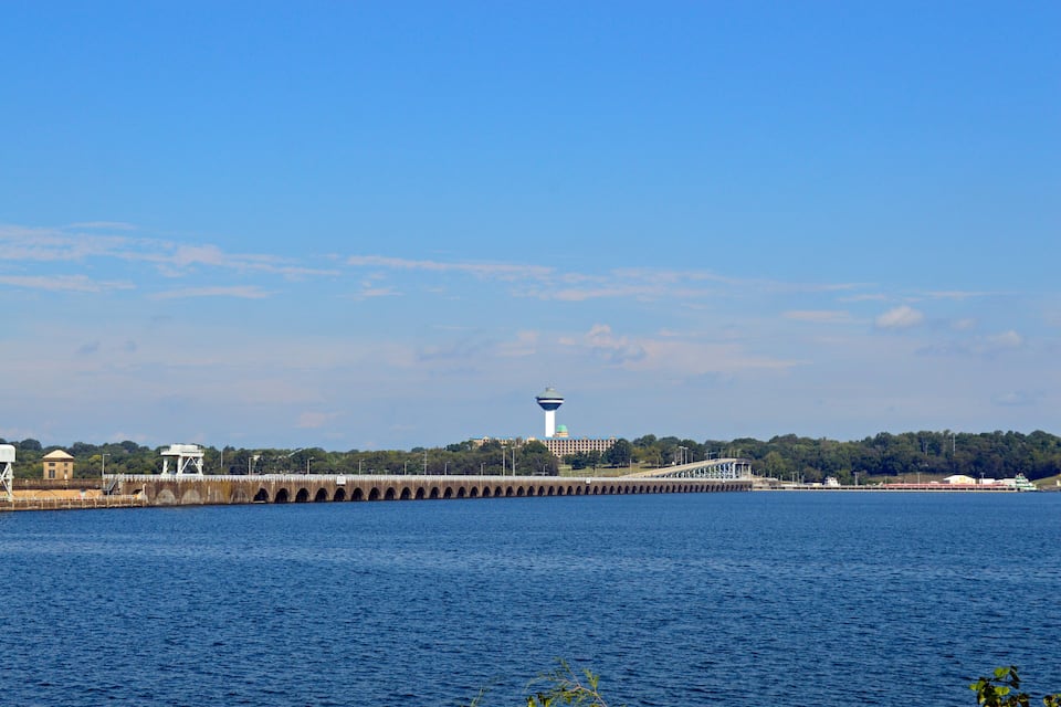 A pier extending into a body of water with a tower and a bridge in the background.