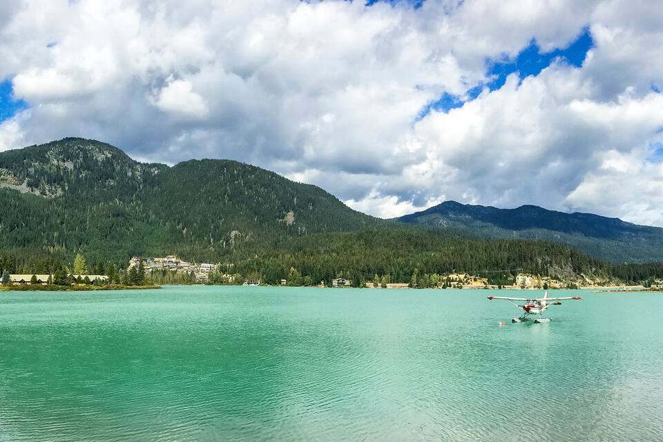 A lake with a small plane on the water, surrounded by mountains and a village.