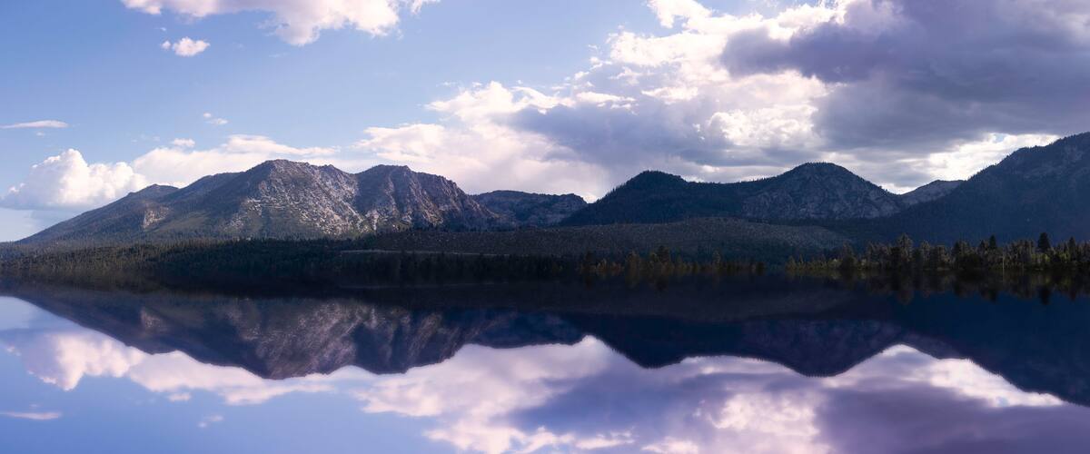 A mountain range reflected in a calm lake with scattered clouds.