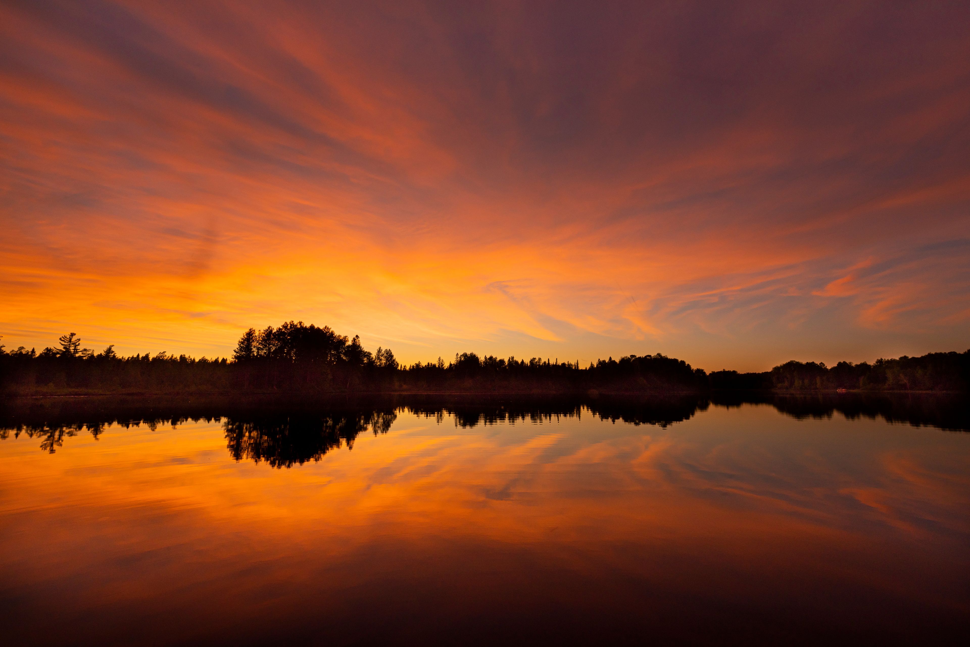 A sunset over a calm lake with a forested shoreline.