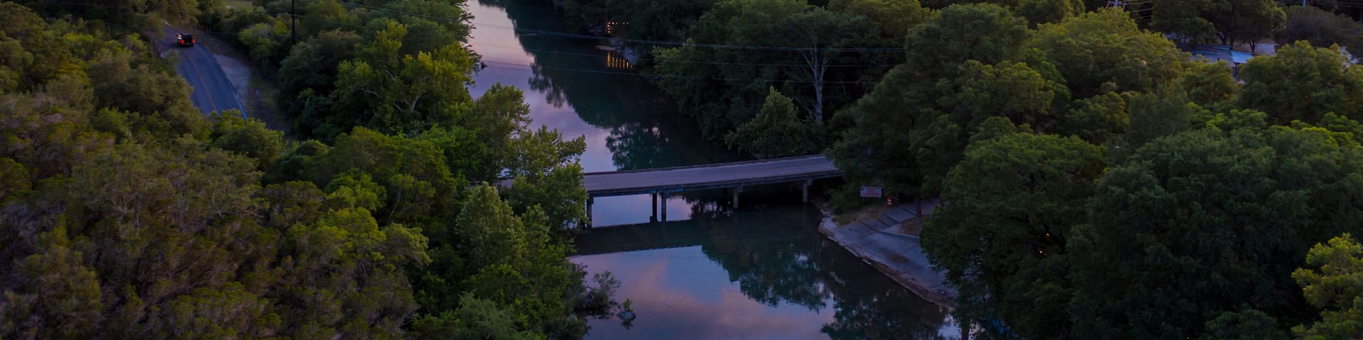 A river winding through a forested valley with hills in the background and a bridge crossing the river.