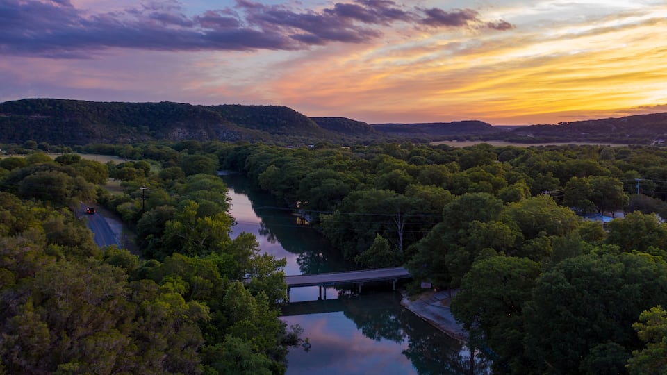 A river winding through a forested valley with hills in the background and a bridge crossing the river.