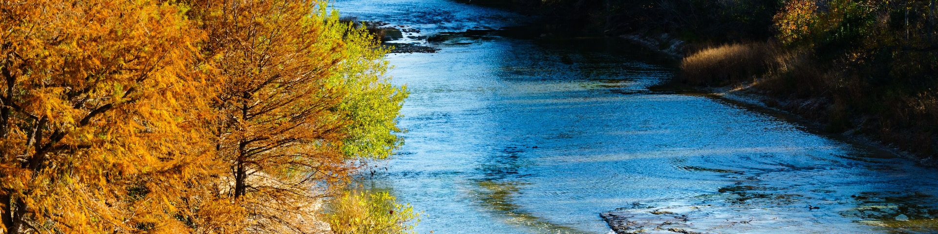 Une rivière qui traverse une forêt aux arbres aux couleurs automnales.