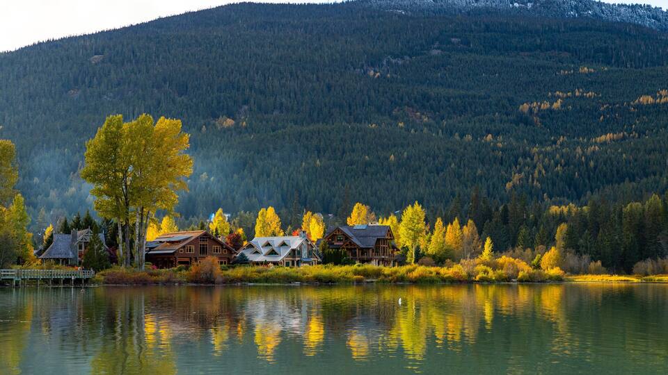 A lakeside cabin community with autumn foliage and a forested mountain backdrop.