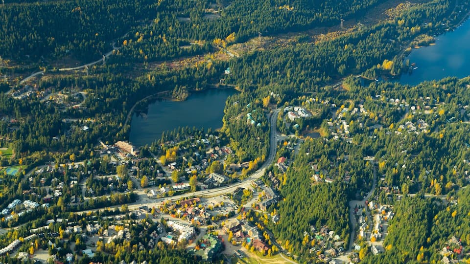 An aerial view of a lakeside town with dense forests, a winding road, and a large body of water.