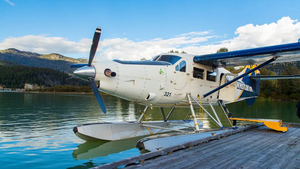 A seaplane docked at a wooden pier with a mountainous backdrop.