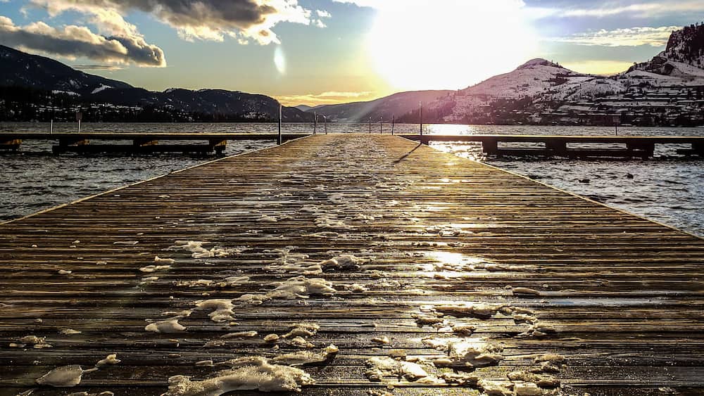 A wooden pier extending into a body of water with mountains in the background and a partly cloudy sky.