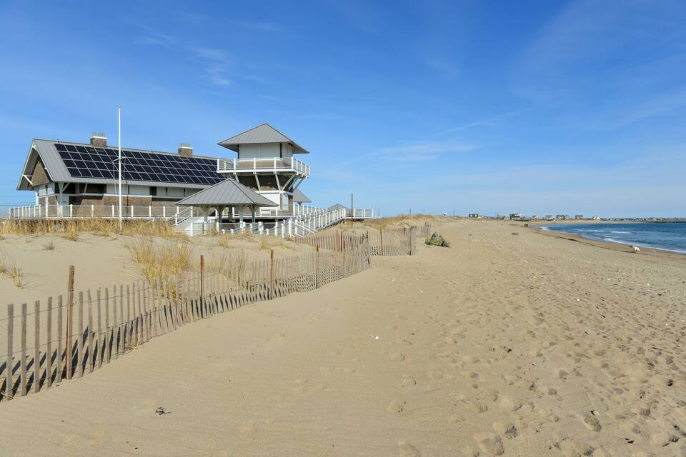 Une maison de plage dotée de panneaux solaires, d’une clôture en bois et surplombant un ciel bleu azur.