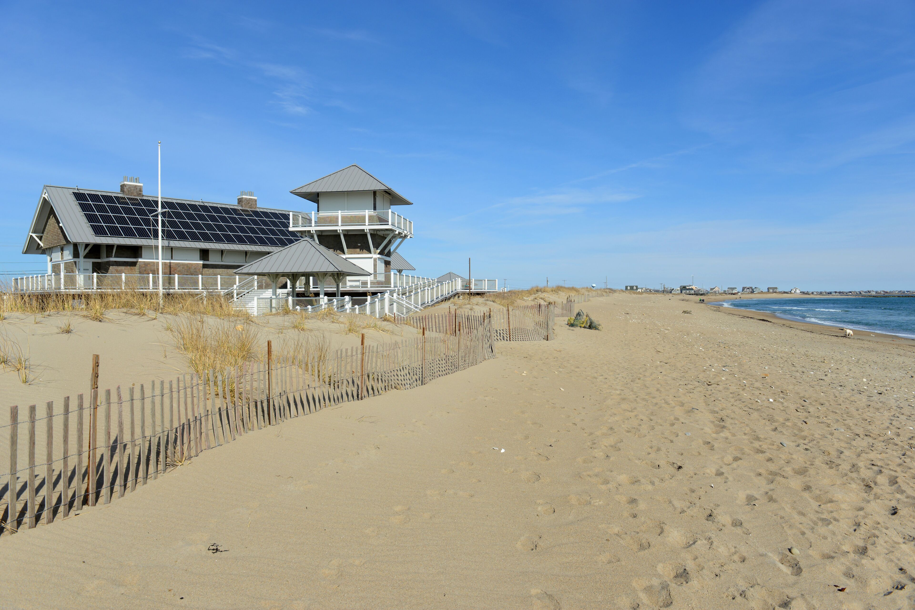 A beach house with solar panels, a wooden fence, and a clear blue sky.