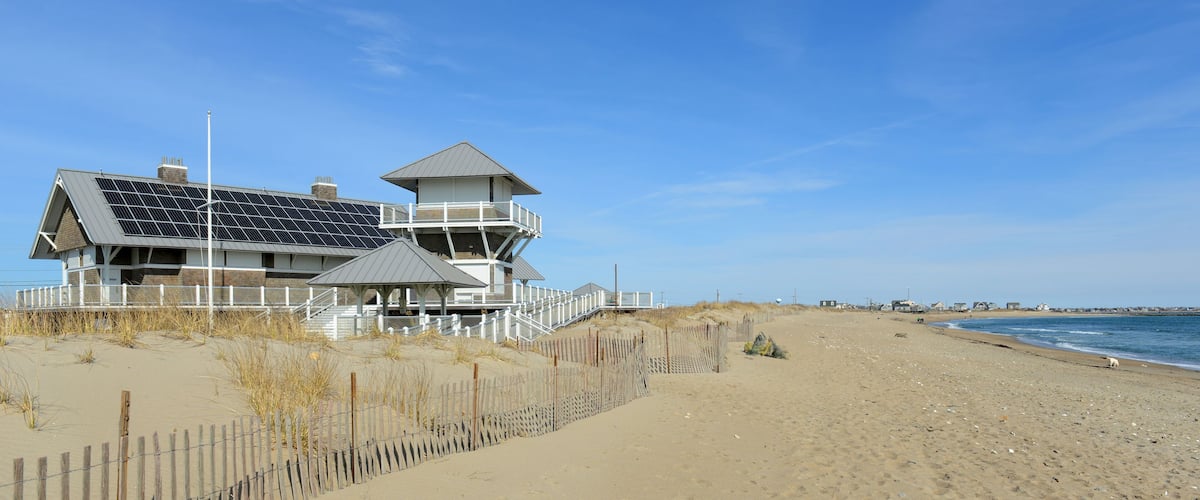 A beach house with solar panels, a wooden fence, and a clear blue sky.