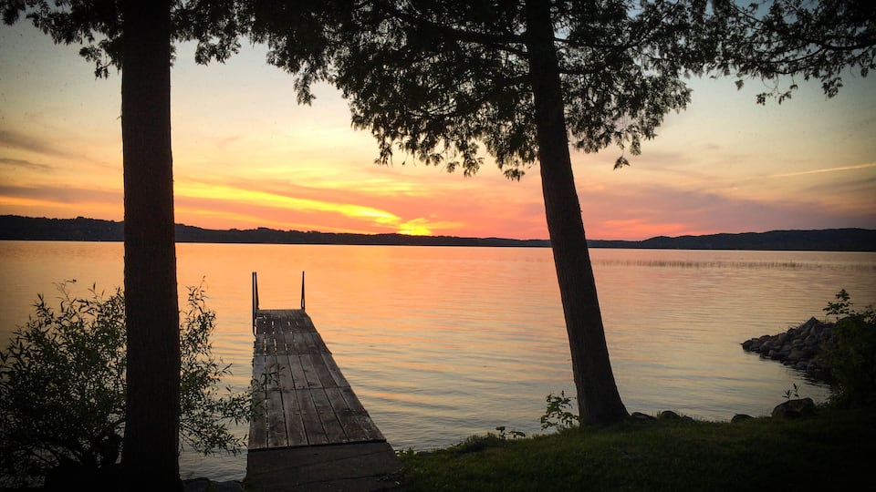 A wooden dock extending into a calm lake at sunset with trees framing the view.