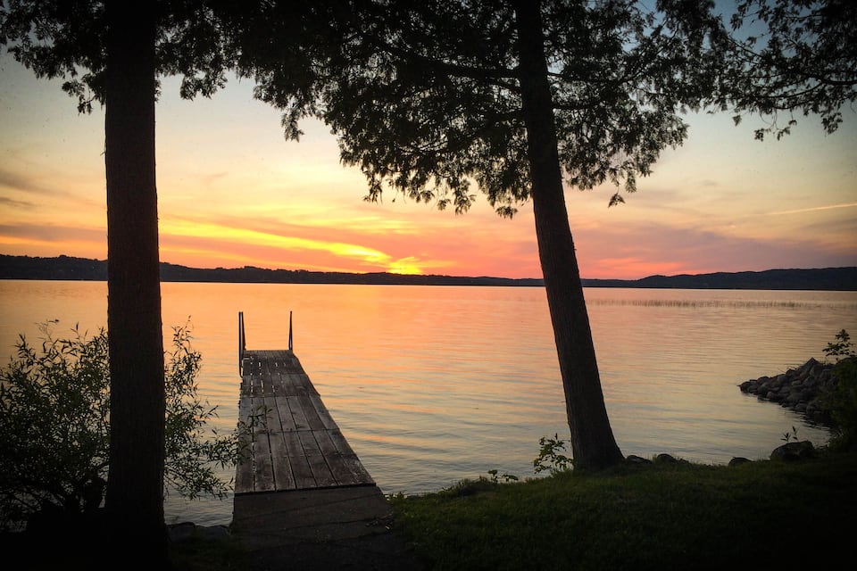A wooden dock extending into a calm lake at sunset with trees framing the view.