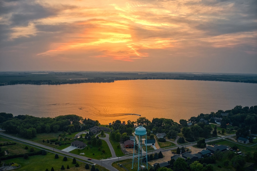 Un atardecer sobre un lago con una torre de agua y una zona residencial.