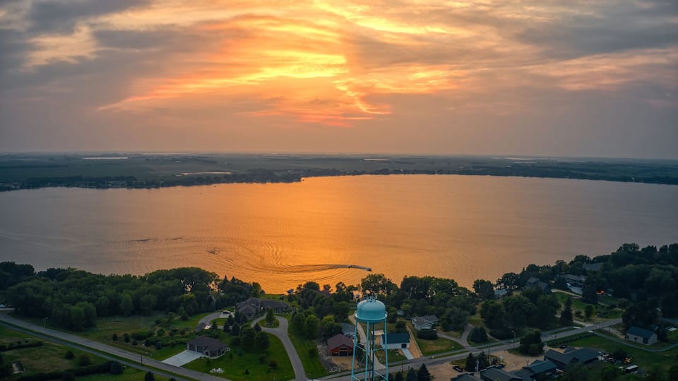A sunset over a lake with a water tower and residential area.