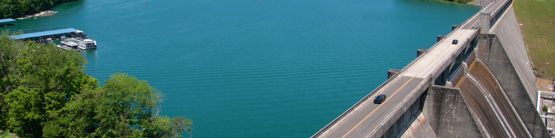 Ein Stausee mit einer Straße auf der Spitze, einem großen See und bewaldeten Hügeln ringsum.