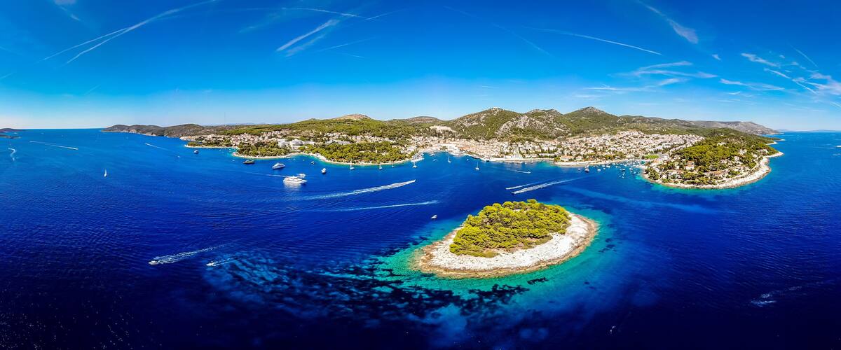 An aerial view of a coastal town with a bay, boats, and a small island with dense greenery.