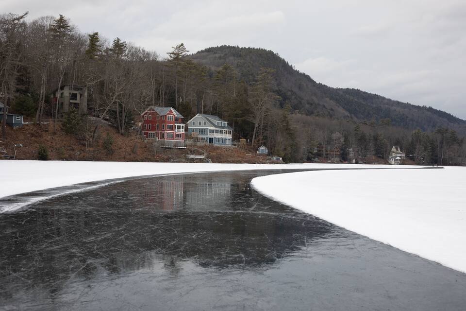 A frozen lake with a house and forested hill in the background.