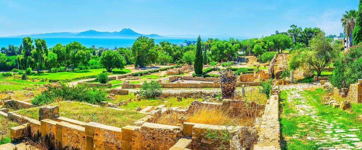 Ancient ruins with a view of the sea and mountains in the background.