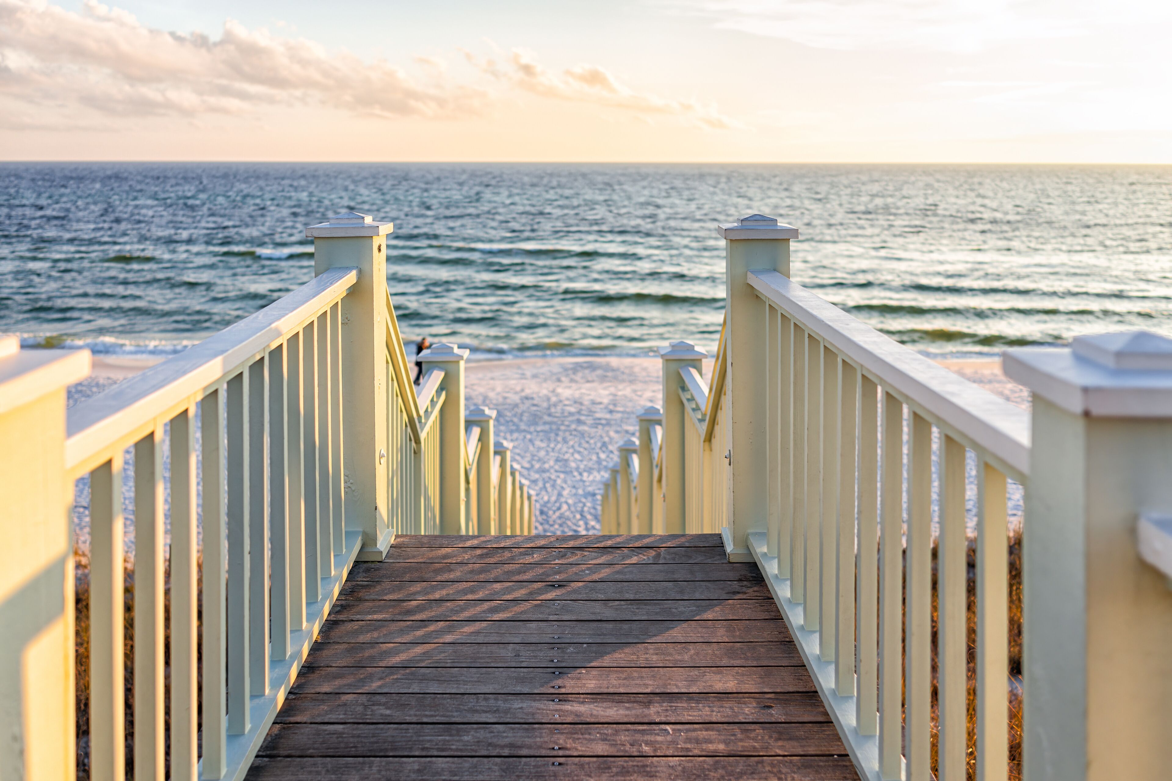 High angle framing view of wooden yellow green white pavilion boardwalk railing stairs steps leading to beach at Gulf of Mexico in Seaside, Florida panhandle sunset and nobody