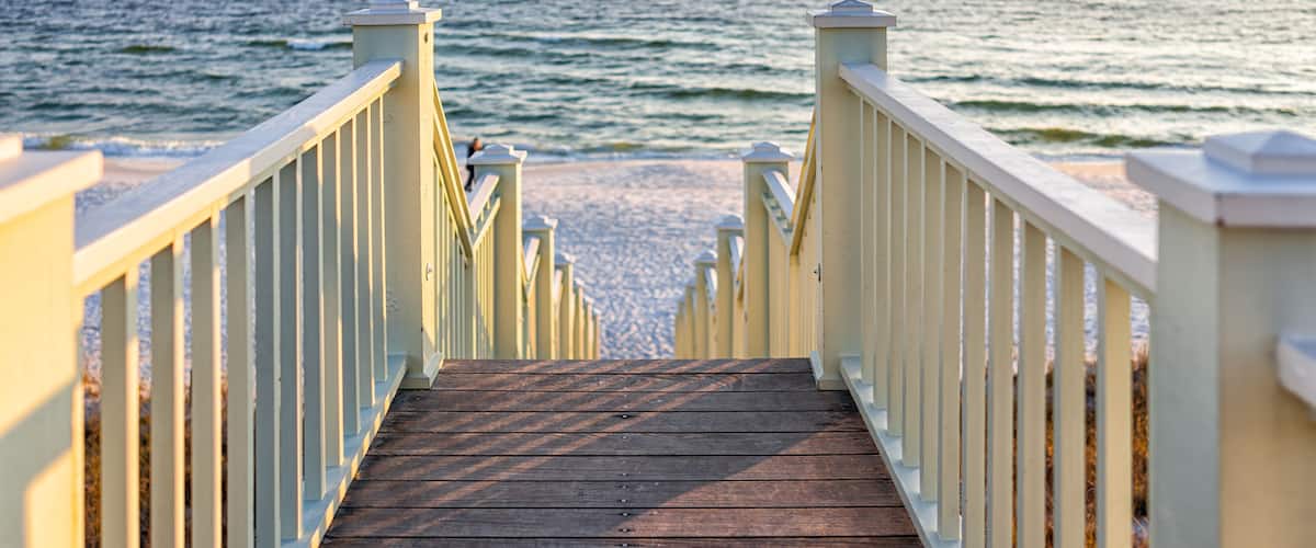 High angle framing view of wooden yellow green white pavilion boardwalk railing stairs steps leading to beach at Gulf of Mexico in Seaside, Florida panhandle sunset and nobody