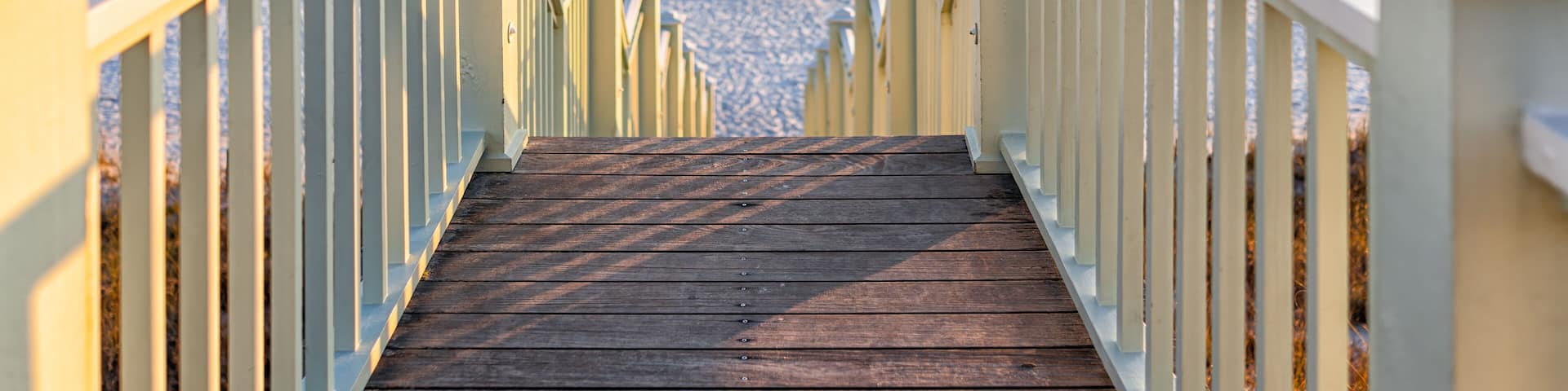 High angle framing view of wooden yellow green white pavilion boardwalk railing stairs steps leading to beach at Gulf of Mexico in Seaside, Florida panhandle sunset and nobody
