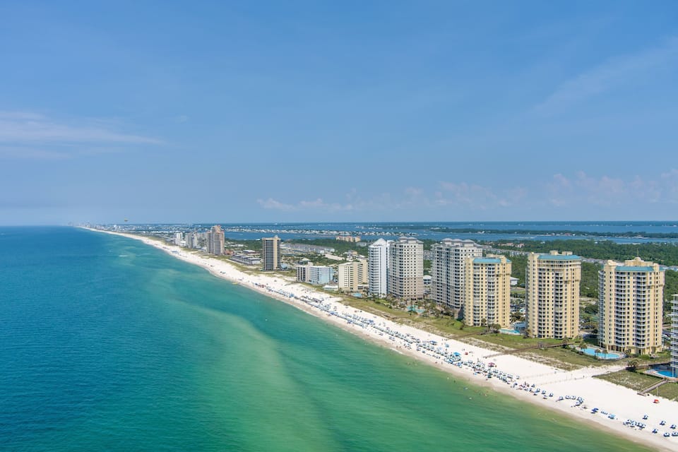 Paisagem costeira com uma extensa praia de areia, hotéis altos e céu azul límpido.