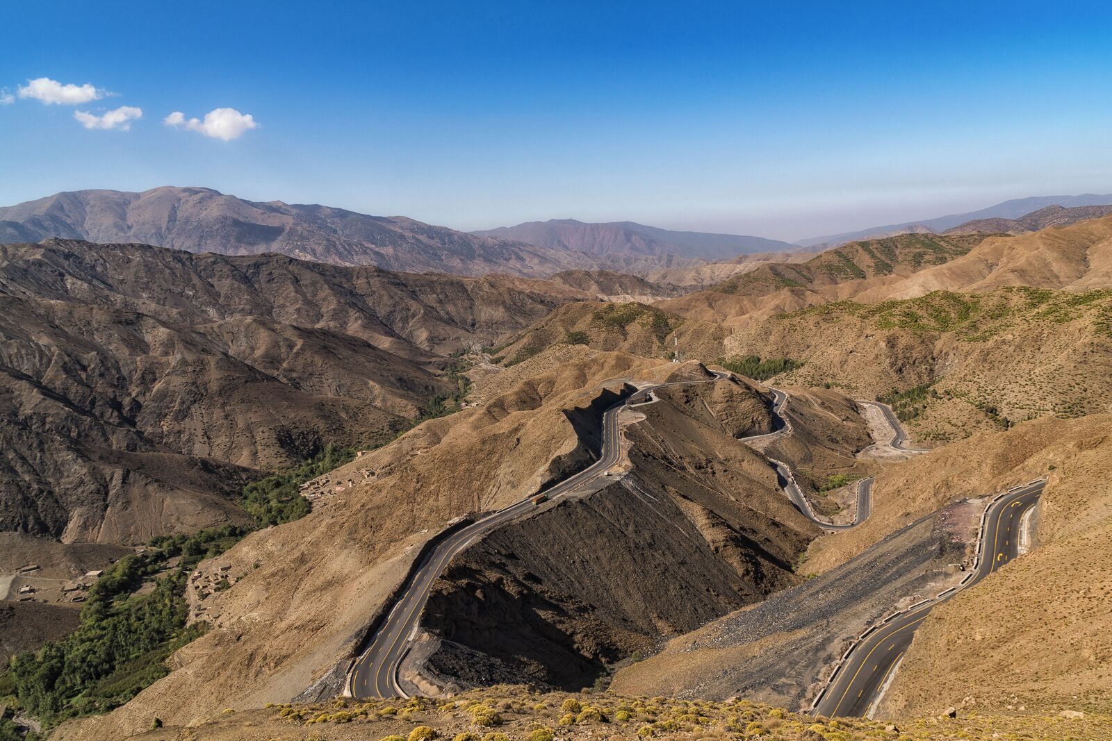 A winding mountain road through a rugged, arid landscape with distant mountain ranges.