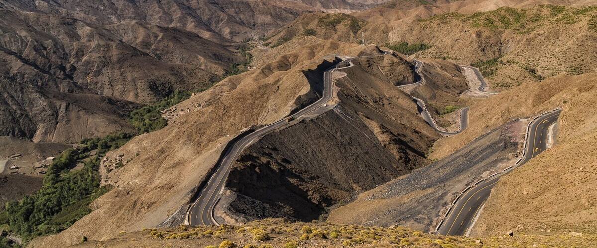 A winding mountain road through a rugged, arid landscape with distant mountain ranges.