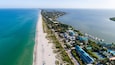 A coastal town with a long beach, clear blue waters, and a marina with boats.