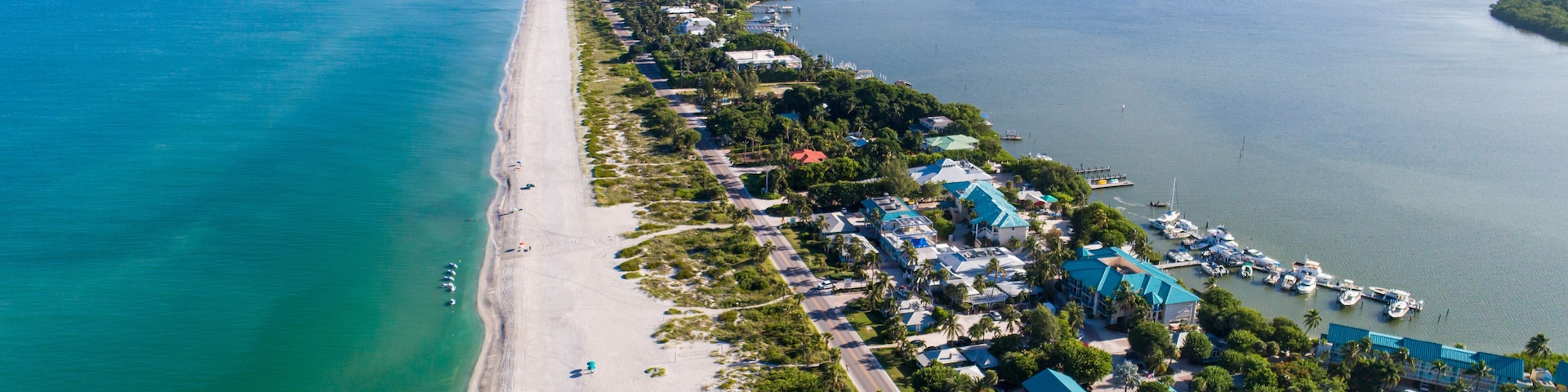 A coastal town with a long beach, clear blue waters, and a marina with boats.