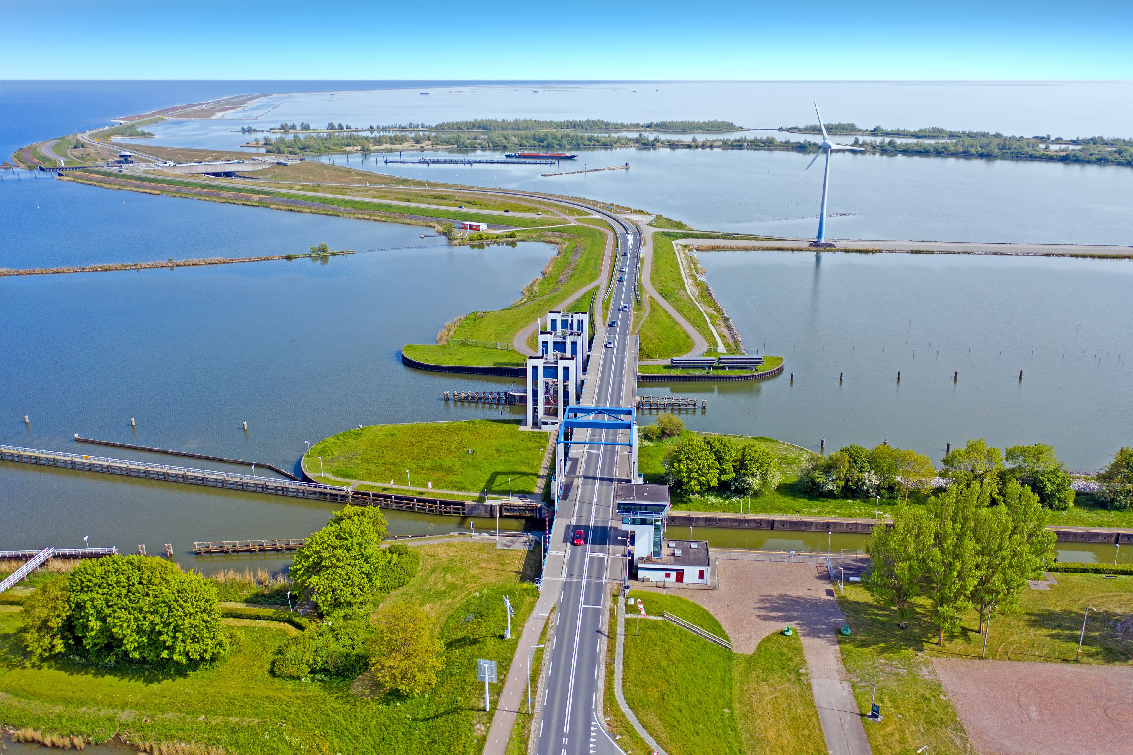 Een brug over een rivier, met een weg eronderdoor, omgeven door groen en water.