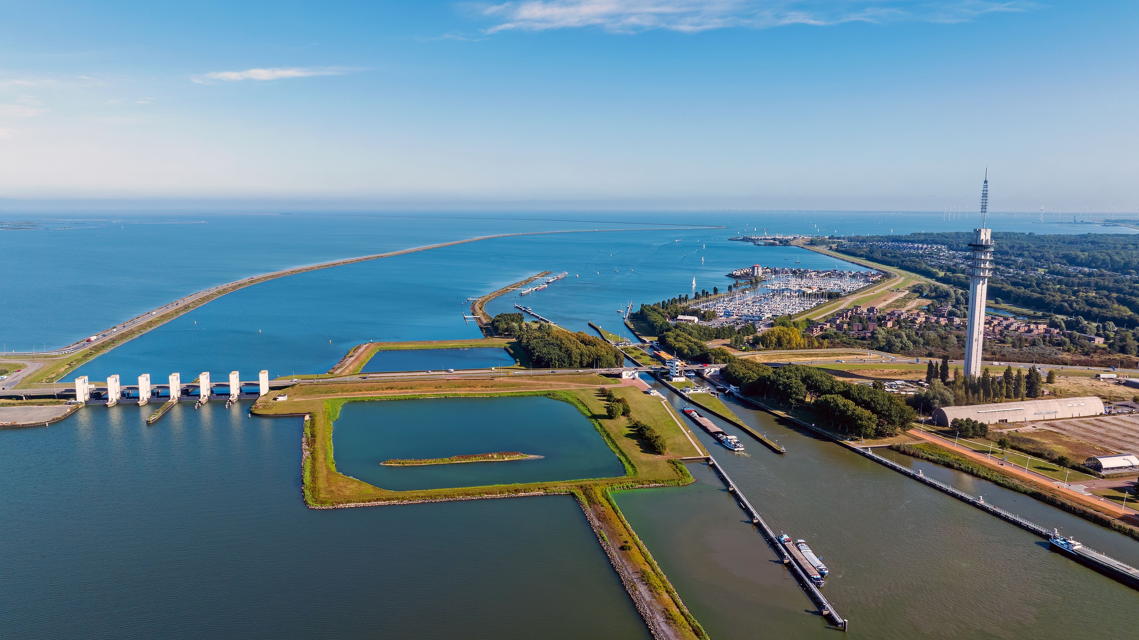 Luchtbeeld van een kuststad met een jachthaven, een vuurtoren en een brede waterweg.