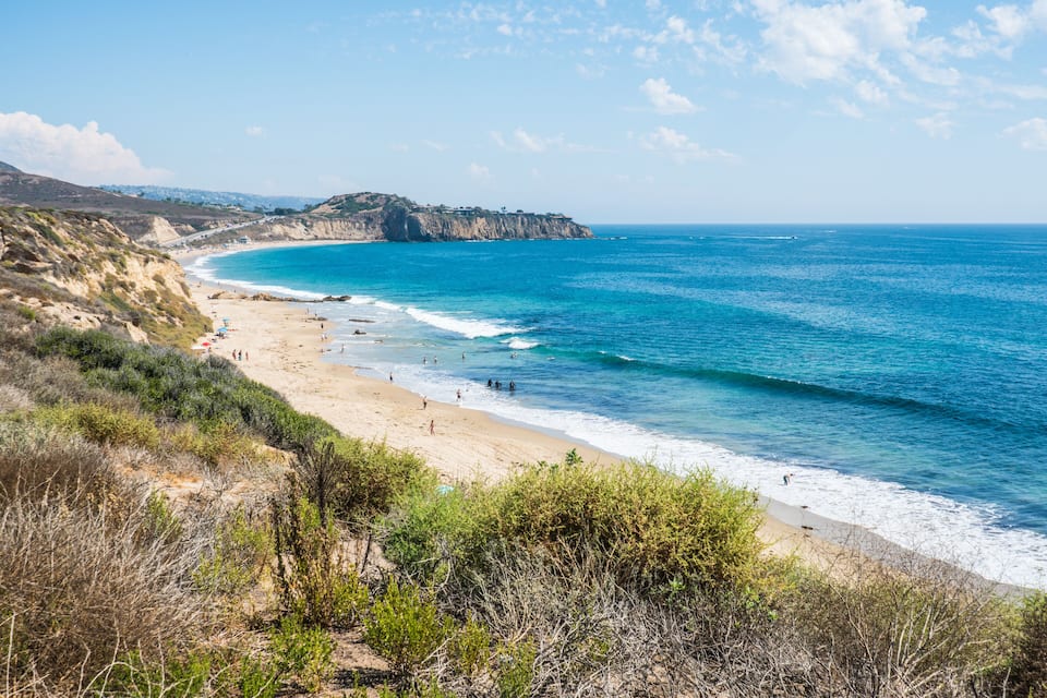 Un paysage côtier avec une plage de sable, une mer bleue et limpide, et des falaises rocheuses.