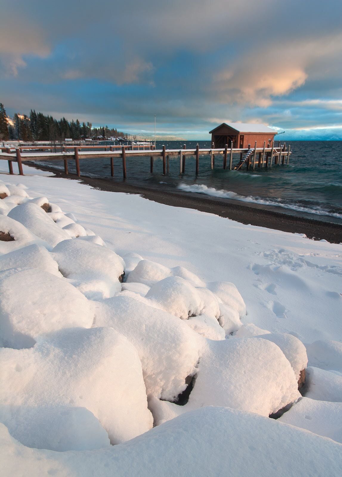 A snow-covered beach with a wooden pier leading to a cabin.
